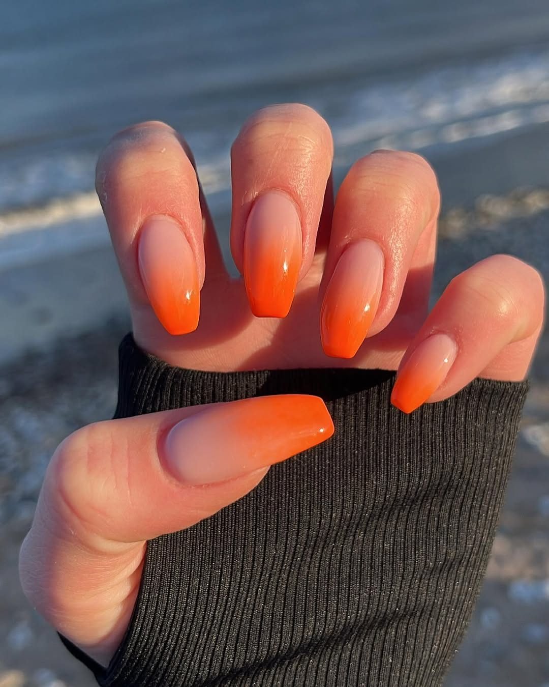 long coffin shaped nails with a bright orange ombre design at the beach
