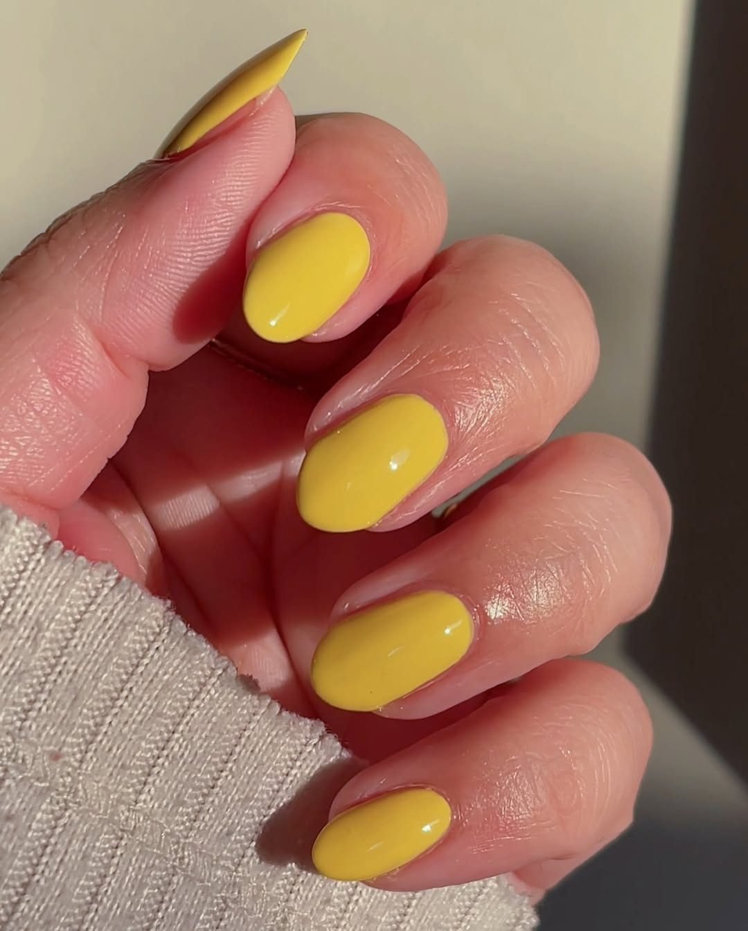 hand showing a solid vibrant yellow summer manicure on short oval nails