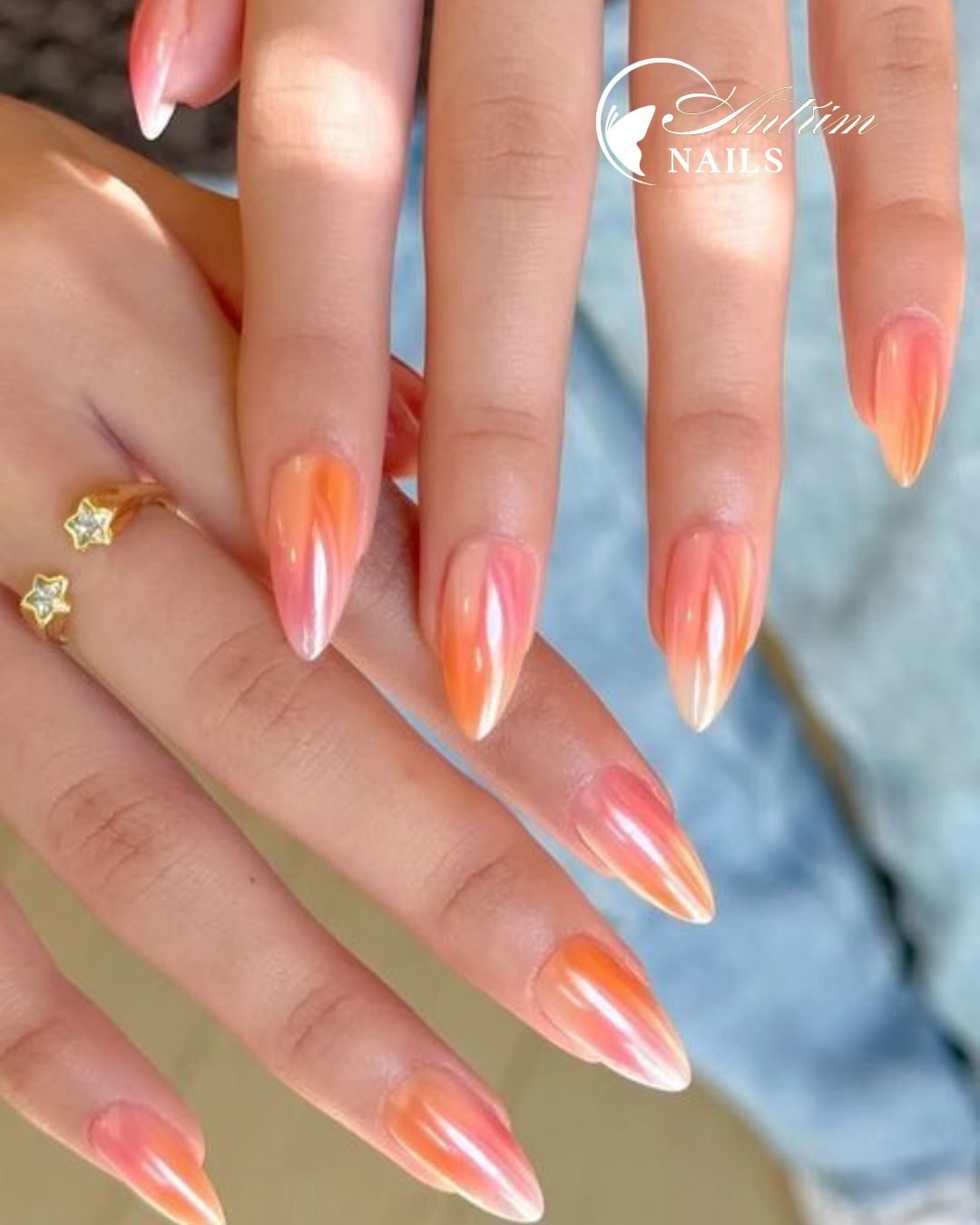 long almond shaped nails with an orange and pink iridescent chrome finish