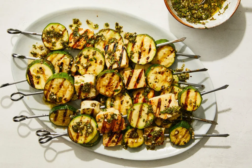 grilled halloumi cheese and zucchini slices on metal skewers over a white platter
