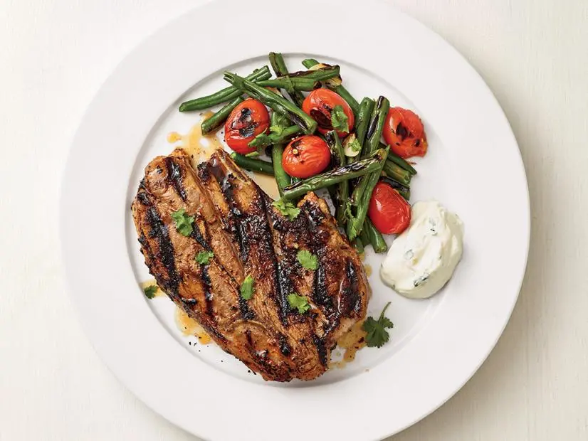 grilled lamb chop served with green beans charred tomatoes and herbed yogurt sauce on a plate