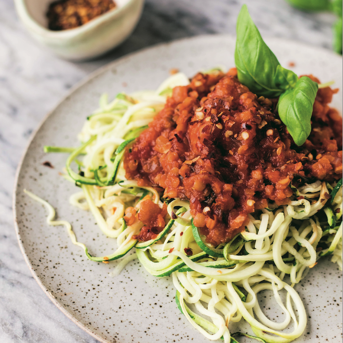 lentil bolognese sauce over spiralized zucchini noodles topped with fresh basil leaves