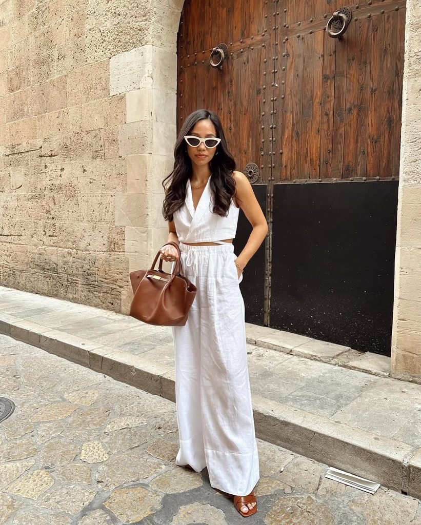 woman in white linen halter top and matching wide leg pants holding brown handbag