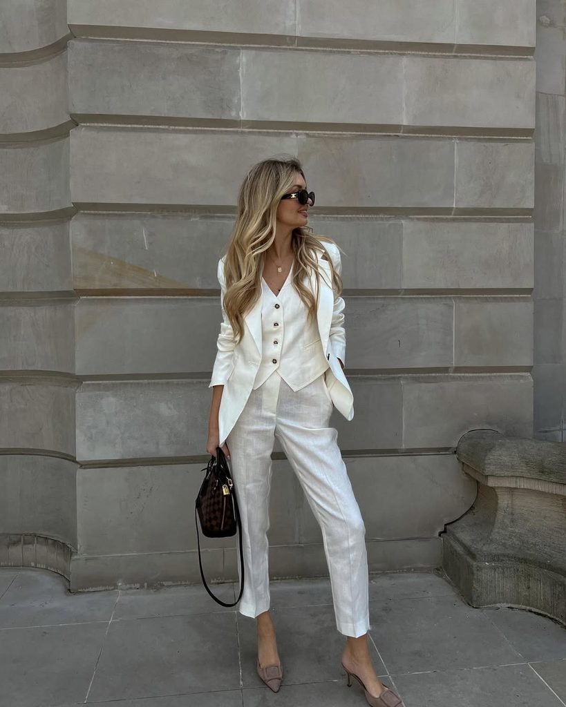 woman wearing three piece white linen suit and sunglasses holding a black handbag