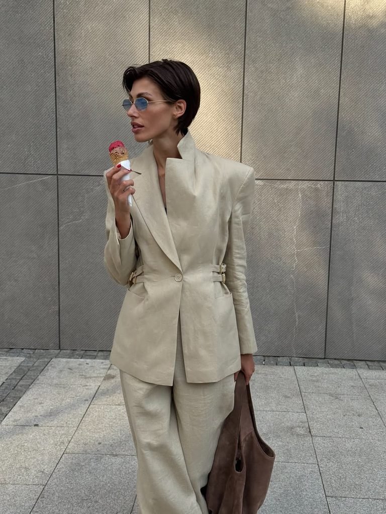 woman wearing beige linen blazer suit holding brown bag while eating ice cream cone