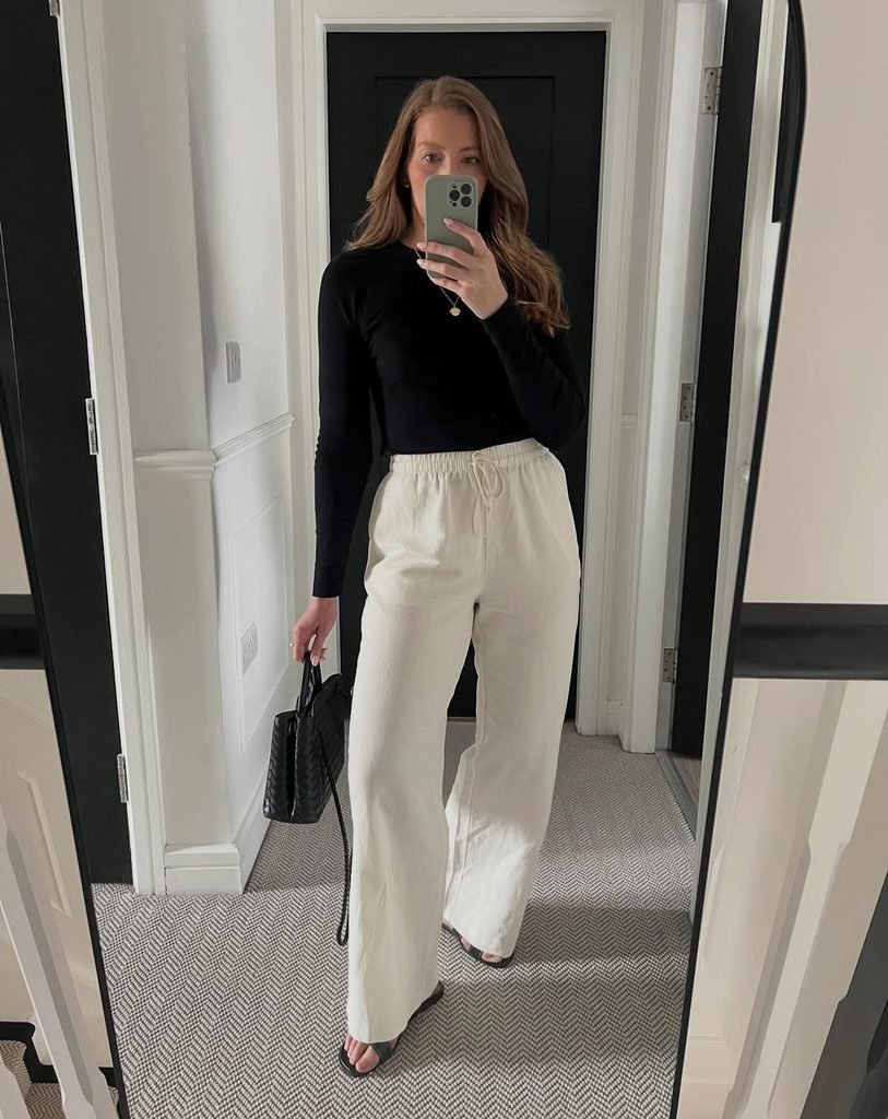 woman in black long sleeve top and cream wide leg linen trousers taking mirror selfie
