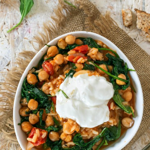 mediterranean chickpea stew topped with a dollop of yogurt and fresh spinach leaves