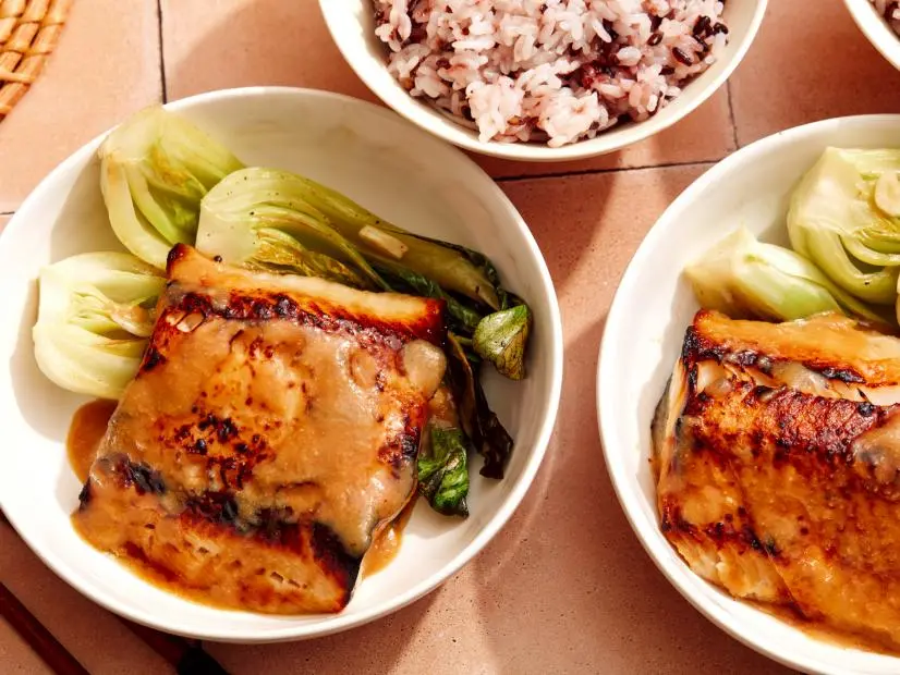 two white bowls of miso glazed cod served with cooked bok choy and rice