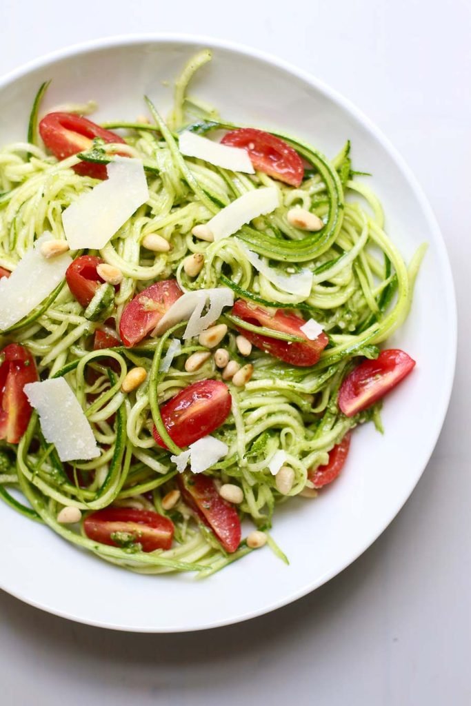 pesto zucchini noodle salad topped with halved cherry tomatoes, pine nuts, and shaved parmesan cheese