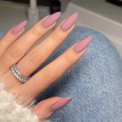 matte dusty rose pink stiletto nails on a hand wearing silver rings
