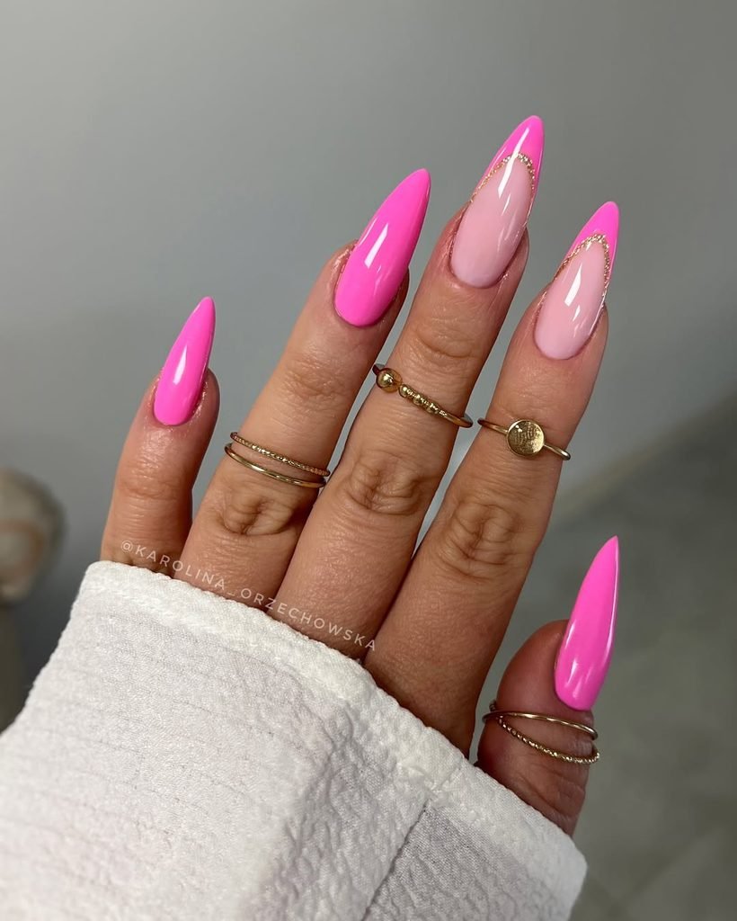 long stiletto nails with bright pink tips, gold glitter accents, and rings