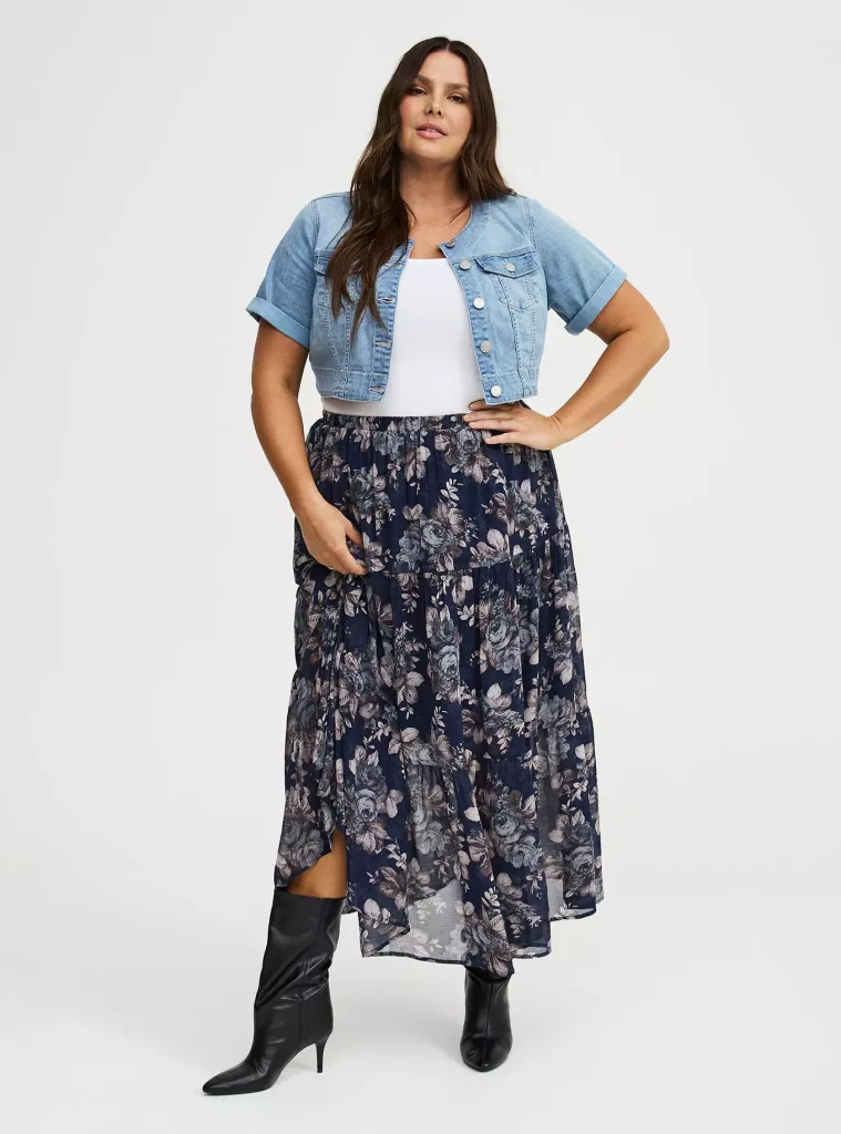 woman wearing a short-sleeved denim jacket, white top, floral maxi skirt, and black boots