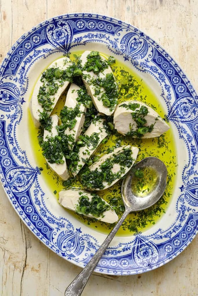 sliced poached chicken breast coated in fresh green herb oil on a patterned platter