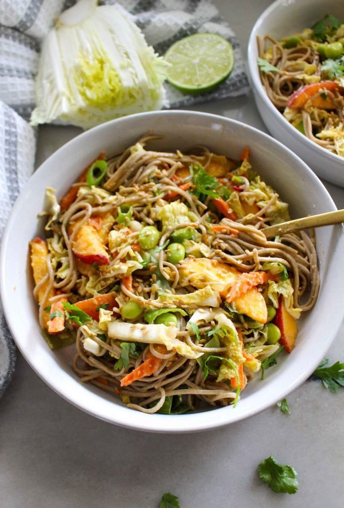 soba noodle salad with edamame, cabbage, carrots, and sesame seeds in a white bowl