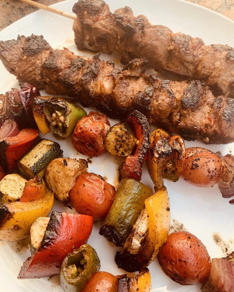 spicy lamb kabobs on skewers with grilled tomatoes, zucchini, and peppers on a plate