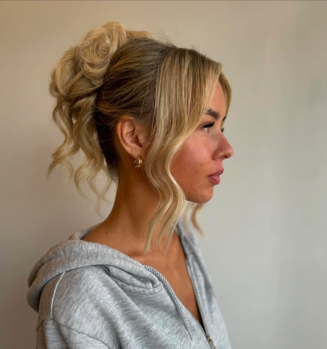 profile of a woman with blonde hair in a messy high bun and face-framing waves