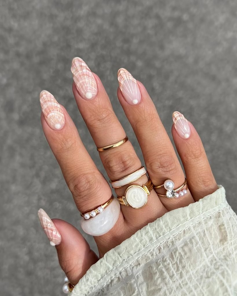 textured seashell nail art on almond nails decorated with gold and pearl rings