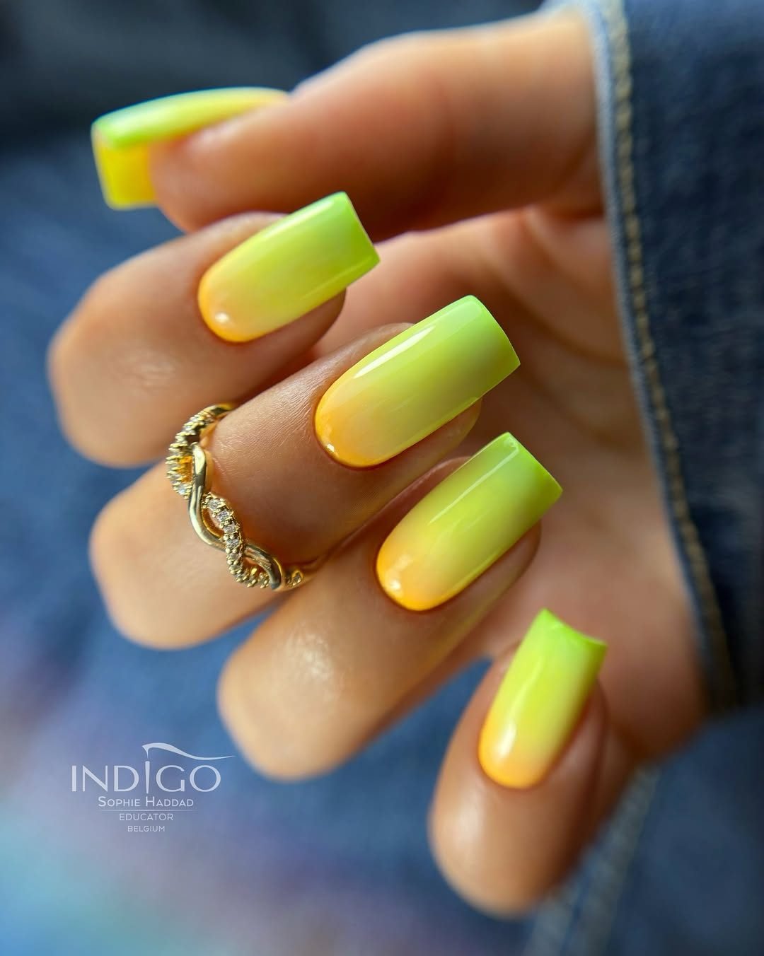 hand with a gold ring displaying long square nails with a yellow and green summer ombré design