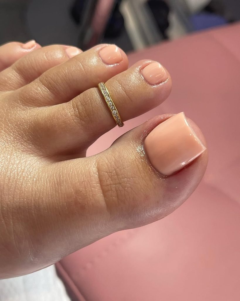 glossy peach nude summer toe nails accented with a sparkling gold rhinestone toe ring