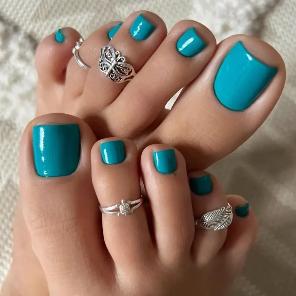 vibrant turquoise teal summer toe nails decorated with stylish silver toe rings