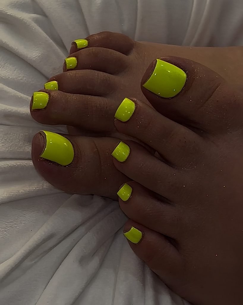 bright neon yellow glittery summer toe nails resting against a soft white blanket