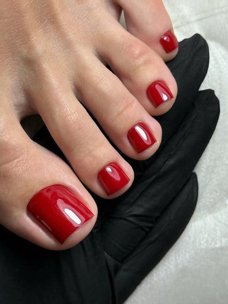 glossy vibrant classic red polish on summer toe nails resting on black fabric