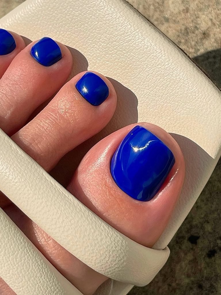 vibrant cobalt royal blue summer toe nails peeking out from white leather sandals