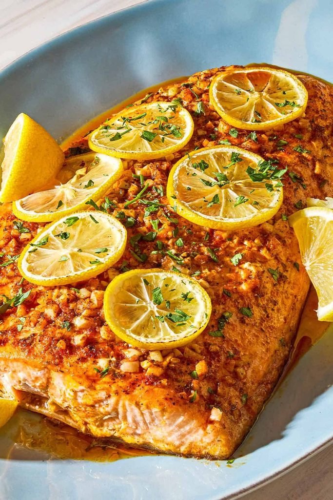 baked lemon garlic salmon fillet topped with fresh lemon slices and minced herbs