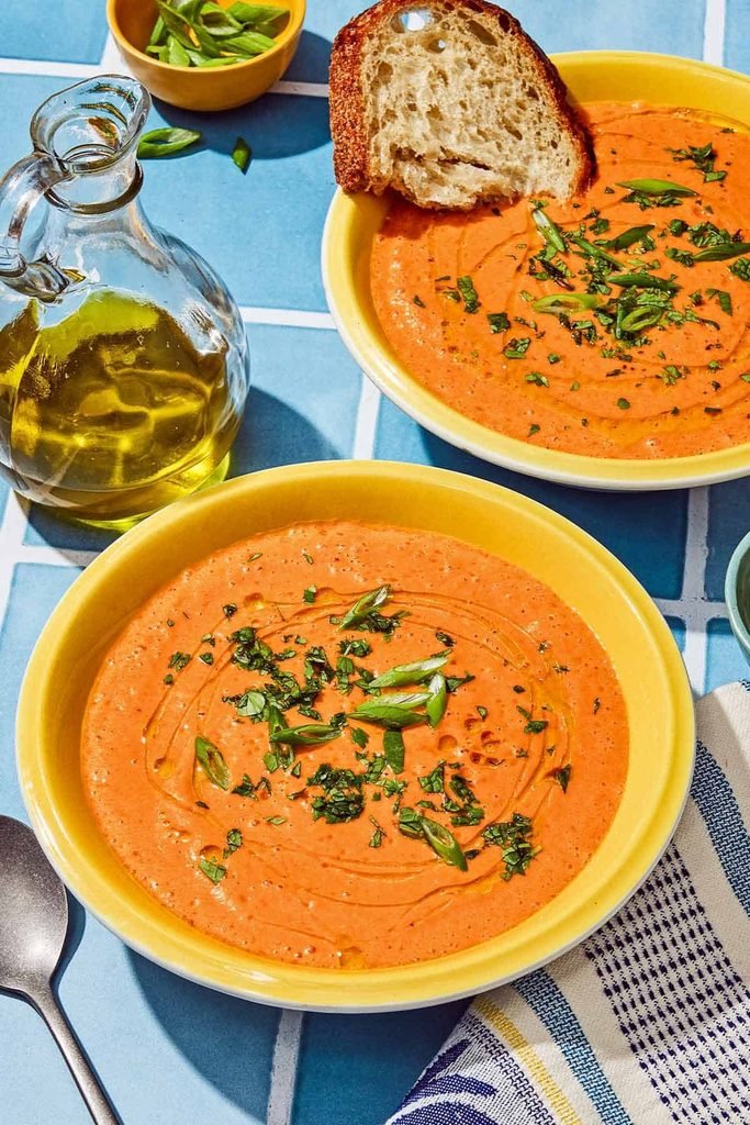 two yellow bowls of chilled gazpacho soup garnished with fresh herbs and olive oil