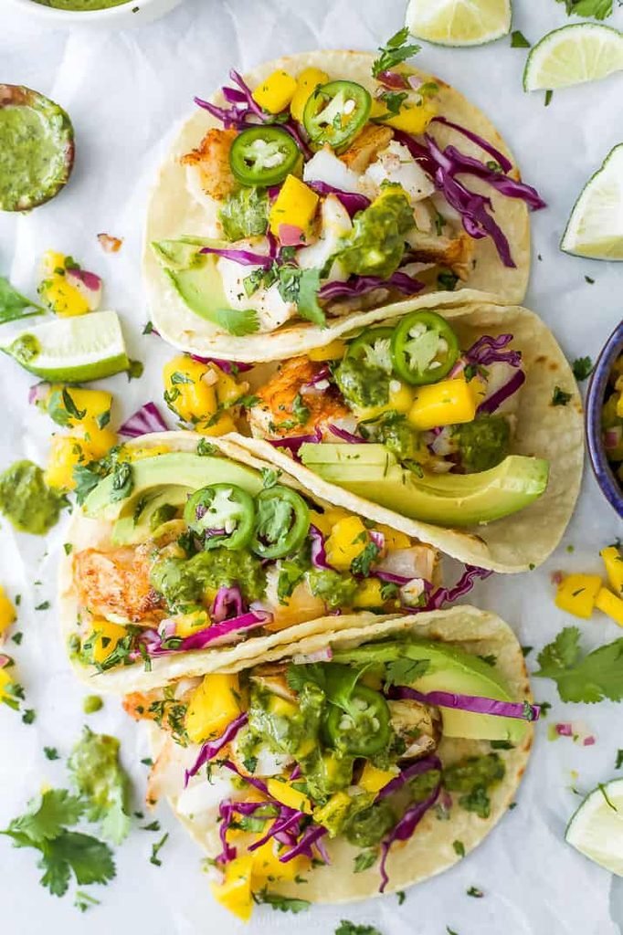 four grilled fish tacos topped with avocado slices, purple cabbage, and mango salsa