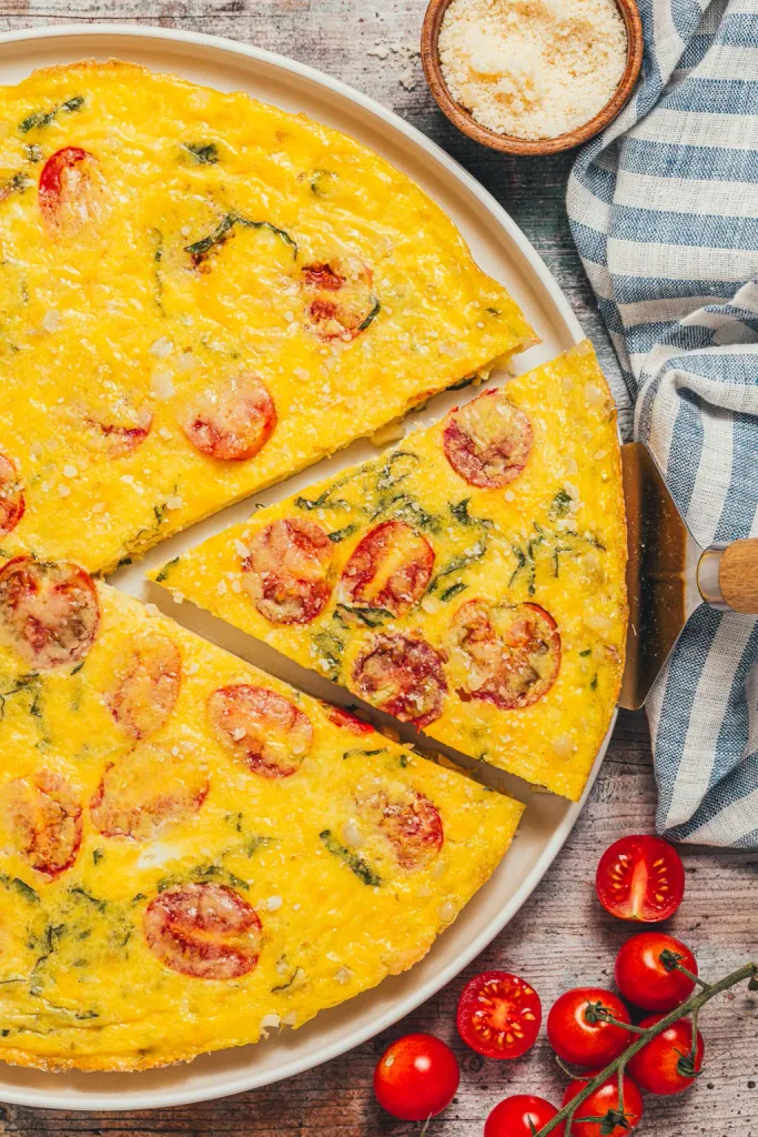 a baked egg frittata with sliced tomatoes and fresh basil on a platter