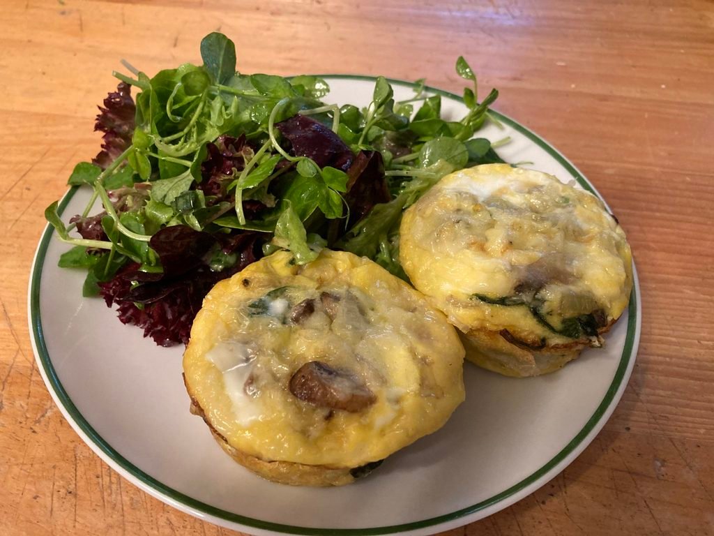 two mini tomato herb frittatas served on a white plate next to a fresh green salad