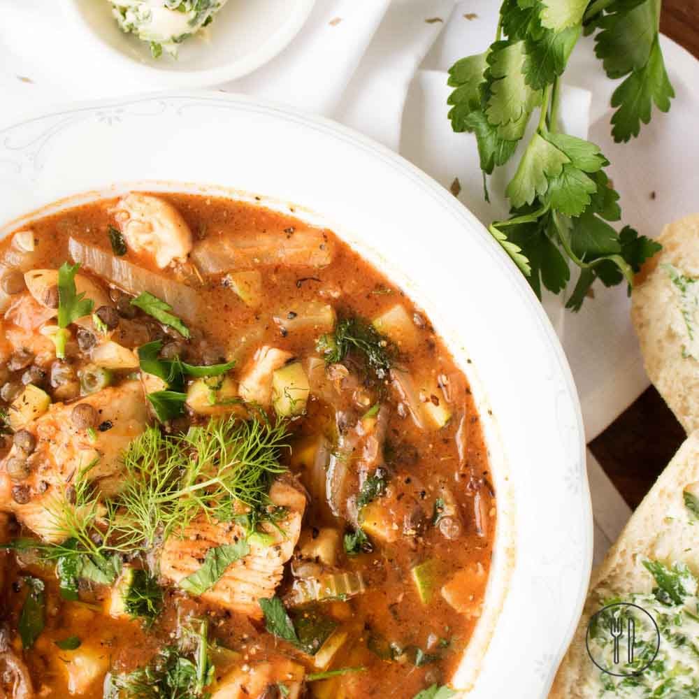 white fish and lentil stew topped with fresh dill and parsley in a bowl