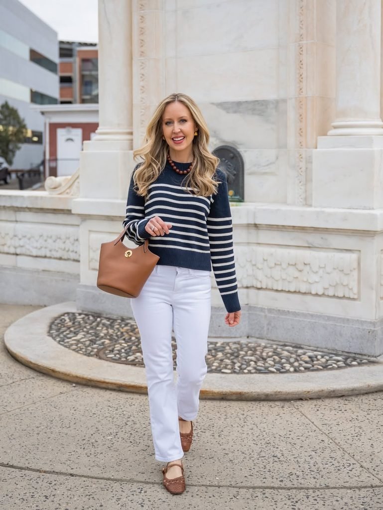 woman in a striped sweater and white jeans walking near a fountain