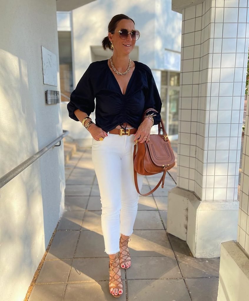 woman in a black blouse and white jeans holding a brown purse
