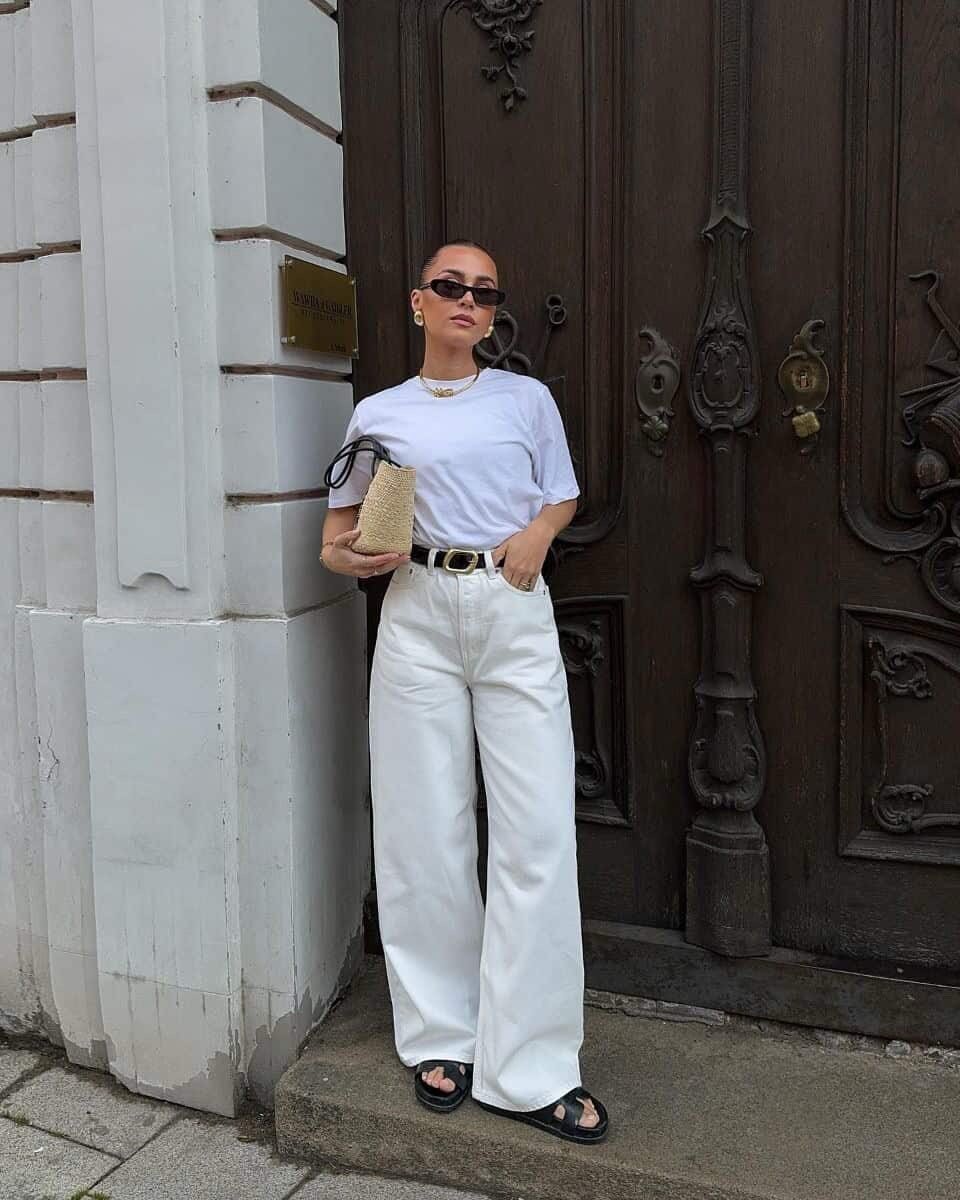 woman wearing a white t-shirt and wide-leg white pants standing in front of a wooden door