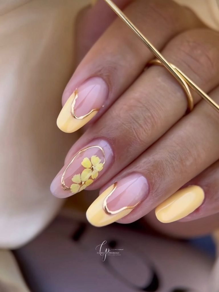 almond nails with a clear base, pastel yellow french tips, and gold metallic accents