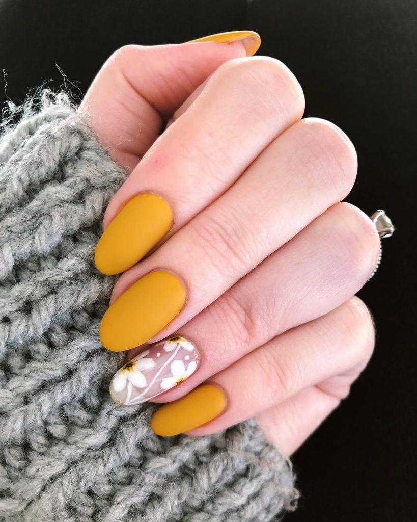 short oval nails painted in matte mustard yellow with white floral accent nail