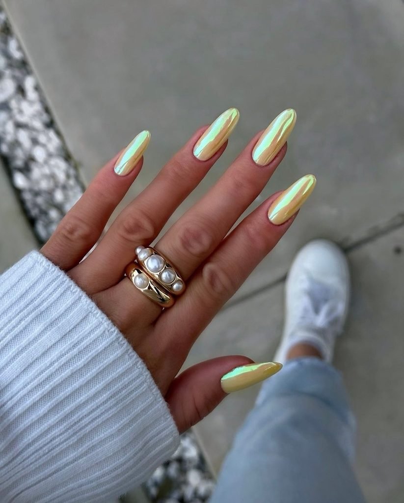 oval shaped nails coated in a shimmering iridescent pale yellow chrome finish