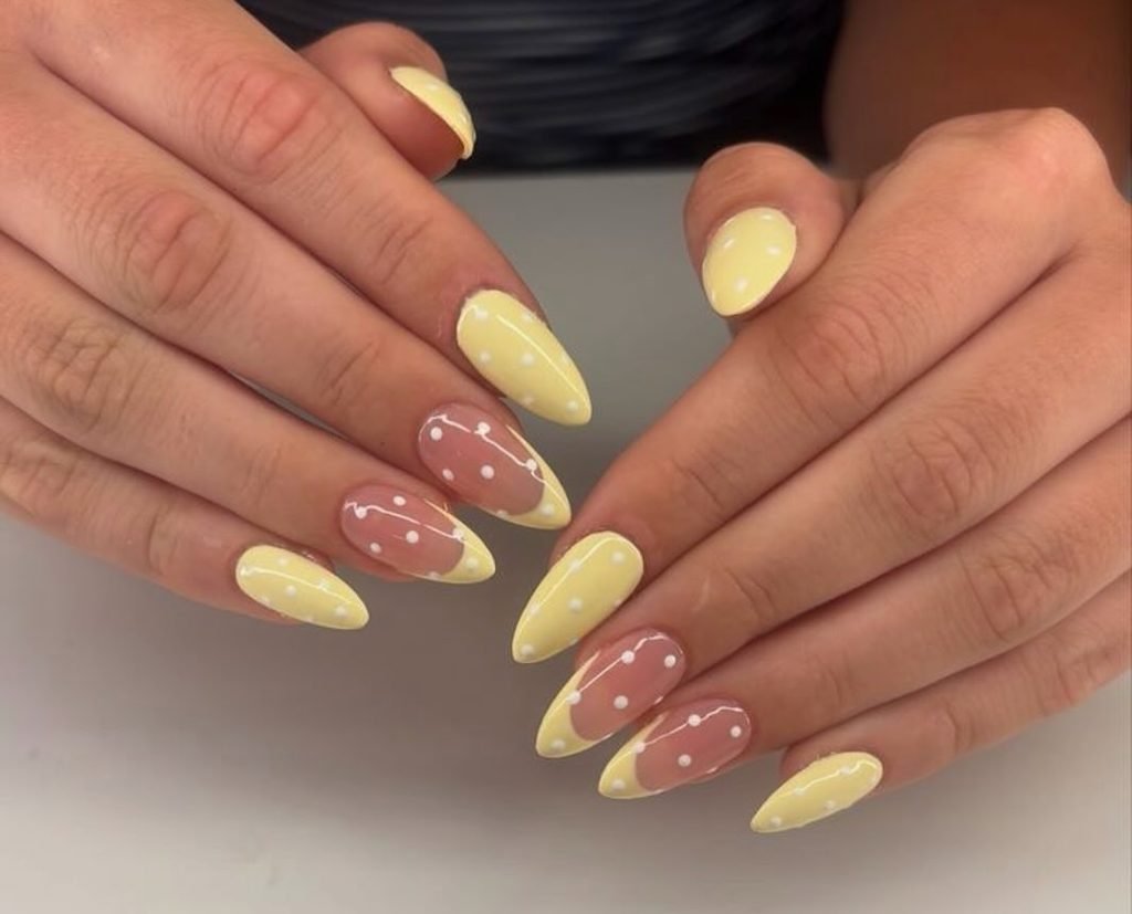 almond shaped nails with yellow polish and french tips decorated with white polka dots