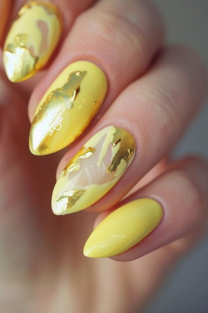 glossy pastel yellow almond nails featuring abstract gold foil accents and clear negative space