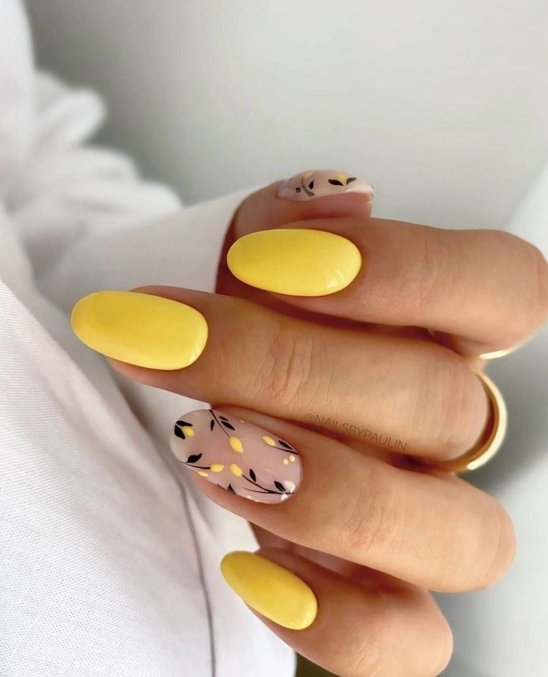 oval yellow nails manicured with black floral branch accent art on a clear base