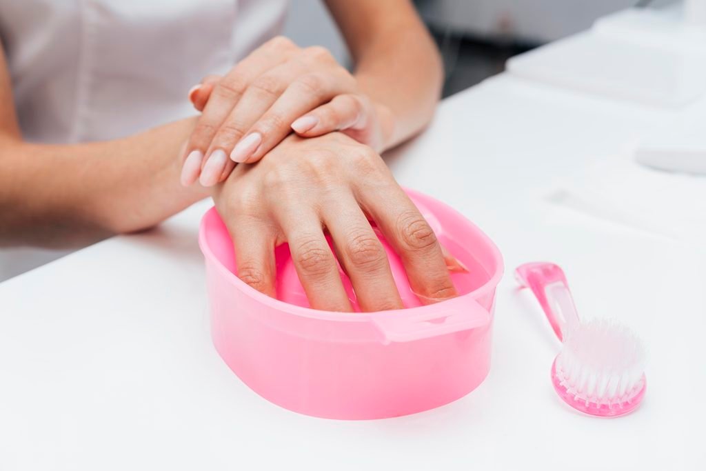 woman soaking her hand in pink manicure bowl with nail brush