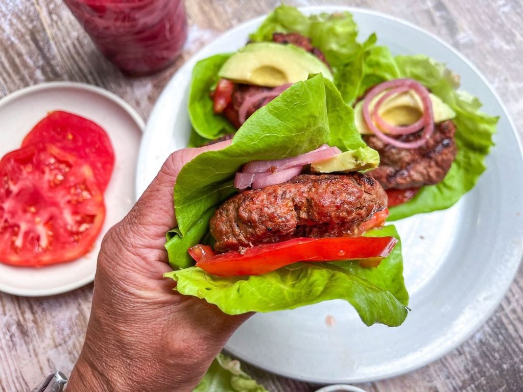 hand holding a lettuce-wrapped bison burger with fresh tomato slices