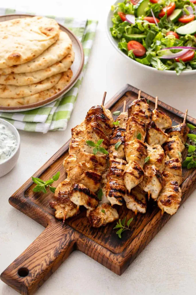 grilled chicken skewers on a wooden board with pita bread and a side salad