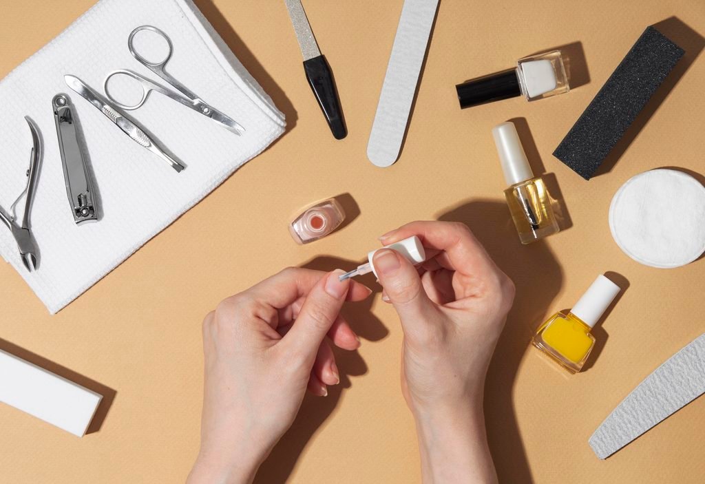 woman applying pink nail polish to her fingernail surrounded by manicure tools