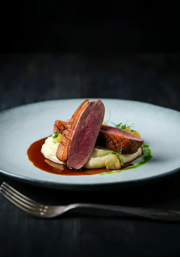 sliced duck breast over celeriac mash with savory reduction sauce on a blue plate