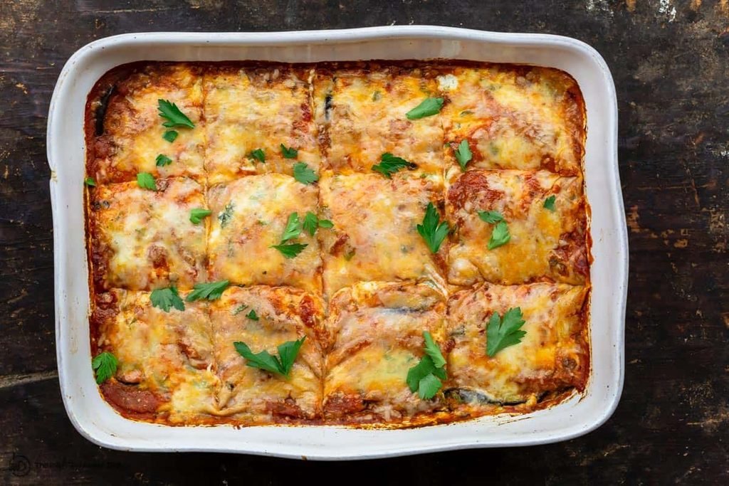 baked eggplant lasagna in a white casserole dish topped with melted cheese and fresh parsley