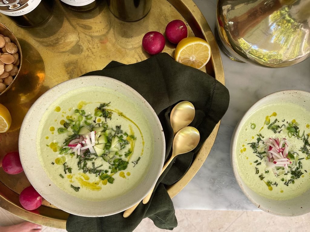 two ceramic bowls of green gazpacho soup garnished with radish matchsticks and oil