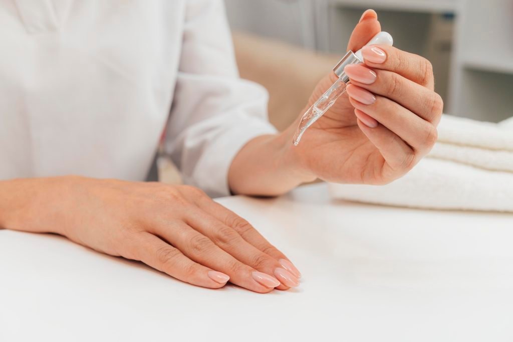 woman with manicured pink nails holding a glass dropper with cuticle oil